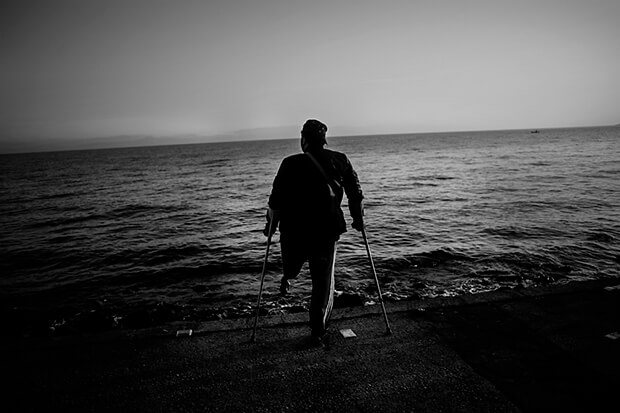 A disabled veteran stands at the beach of Lesbos.