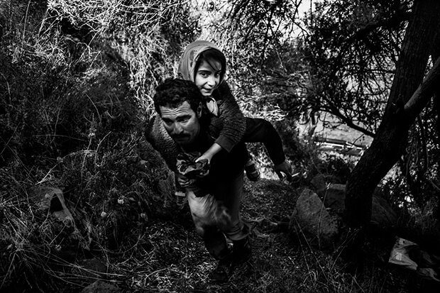 Refugee with his daughter climbs up to a field after arriving from Turkey to Lesbos island, Greece, on a dinghy. They have to walk around 55 kilometers (34 miles) to reach the capital of Lesvos, Mytillini.